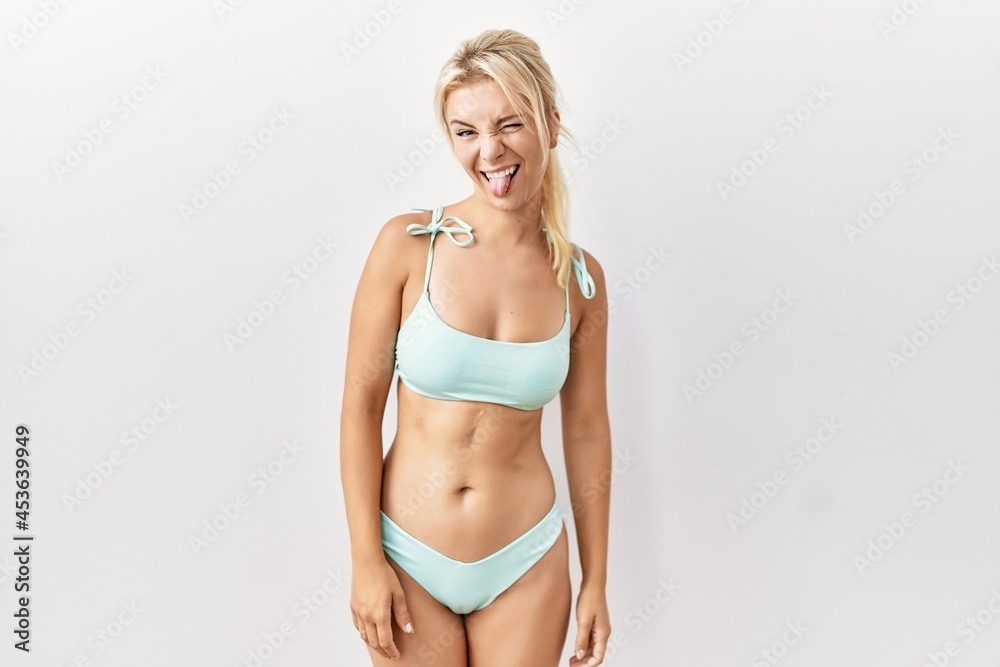 Young caucasian woman wearing bikini over isolated background sticking tongue out happy with funny expression. emotion concept. Young caucasian woman wearing bikini over isolated background sticking tongue out happy with funny expression. emotion concept.