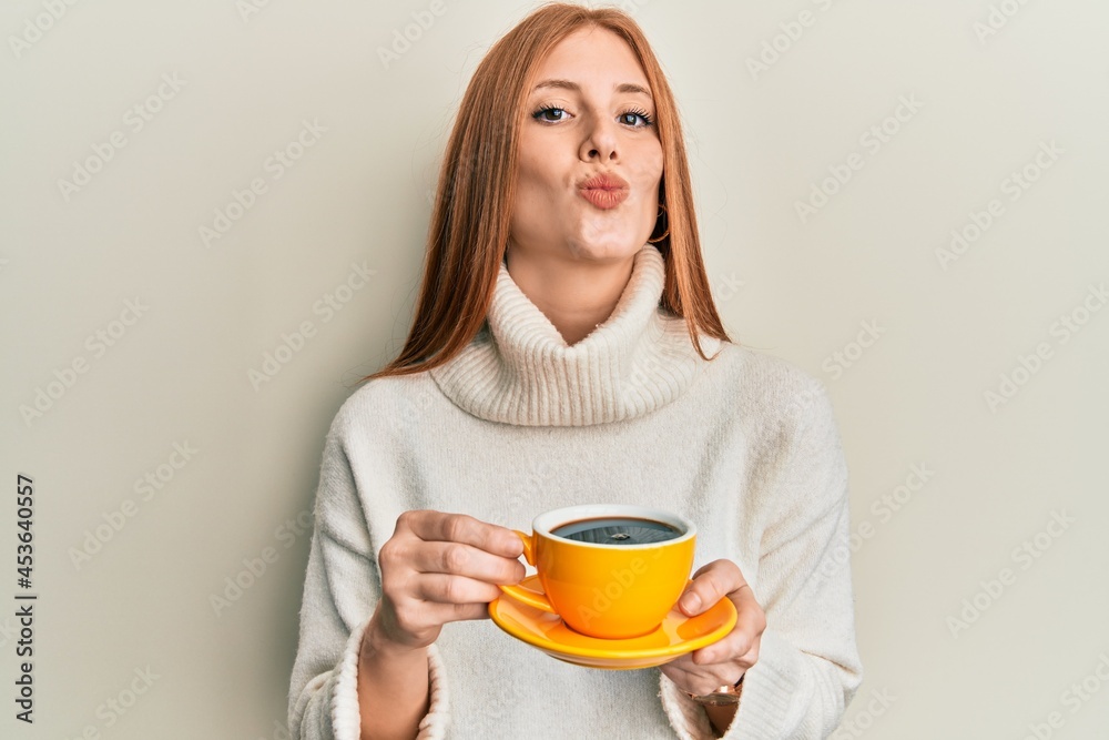Young irish woman drinking a cup of coffee looking at the camera blowing a kiss being lovely and sexy. love expression. Young irish woman drinking a cup of coffee looking at the camera blowing a kiss being lovely and sexy. love expression.