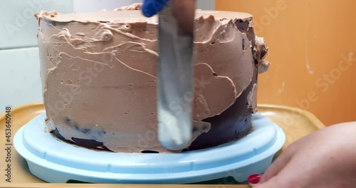 Confectioner woman is smearing cream on sides of cake using spatula, closeup view. culinary, baking and cooking food concept, home cooking
