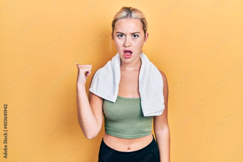 Young blonde girl wearing sportswear and towel surprised pointing with hand finger to the side, open mouth amazed expression. Young blonde girl wearing sportswear and towel surprised pointing with hand finger to the side, open mouth amazed expression.