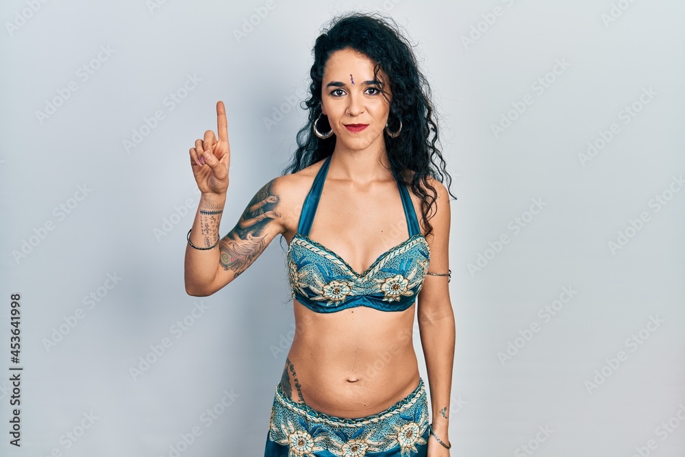Young woman wearing bindi and traditional belly dance clothes showing and pointing up with finger number one while smiling confident and happy. Young woman wearing bindi and traditional belly dance clothes showing and pointing up with finger number one while smiling confident and happy.