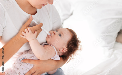 a young mother gives a sick child medicine with the help of a dispenser. the child takes medicine for teething. Treatment