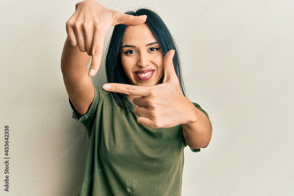 Young hispanic girl wearing casual t shirt smiling making frame with hands and fingers with happy face. creativity and photography concept. Young hispanic girl wearing casual t shirt smiling making frame with hands and fingers with happy face. creativity and photography concept.