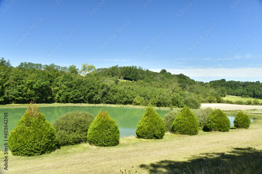 L'étang aux eaux émeraudes entre forêt et prairie sous un ciel d'été près du Bourg de Champagne au Périgord Vert