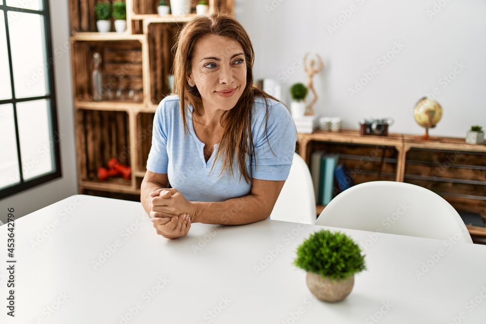 Middle age caucasian woman smiling happy sitting on the table at home.