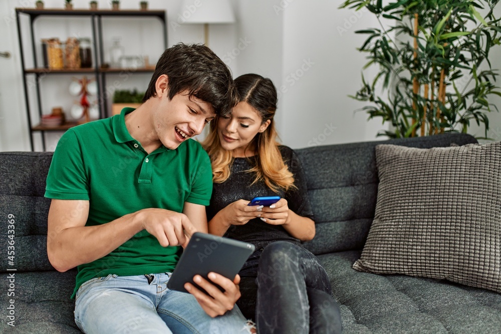 Young caucasian couple smiling happy using touchpad and smartphone at home.