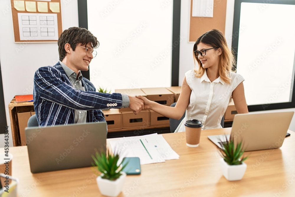 Two business workers smiling happy shaking hands at the office.