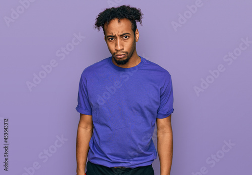 Young african american man with beard wearing casual purple t shirt skeptic and nervous, frowning upset because of problem. negative person.
