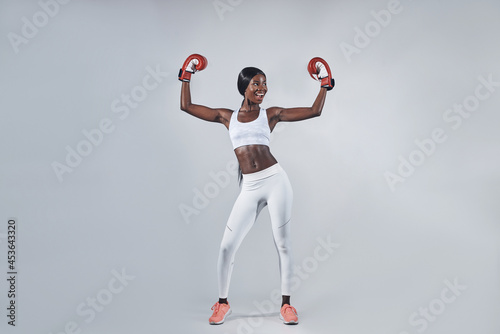Beautiful young African woman in boxing gloves keeping arms raised
