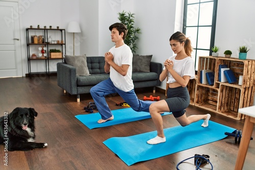 Young caucasian couple concentrate training legs exercise with dog at home.