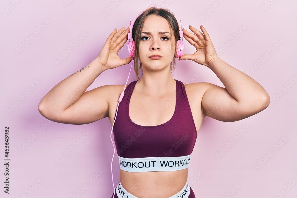 Young hispanic girl wearing gym clothes and using headphones skeptic and nervous, frowning upset because of problem. negative person. Young hispanic girl wearing gym clothes and using headphones skeptic and nervous, frowning upset because of problem. negative person.