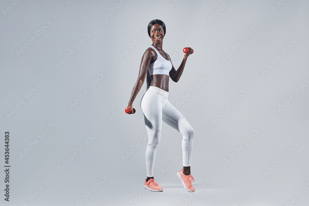 Beautiful young African woman in sports clothing exercising with dumbbells