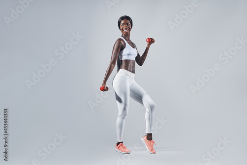 Beautiful young African woman in sports clothing exercising with dumbbells