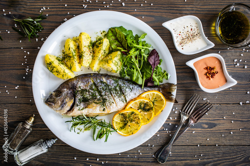 Fotografia Roast sea bream  with potatoes and vegetables on wooden table