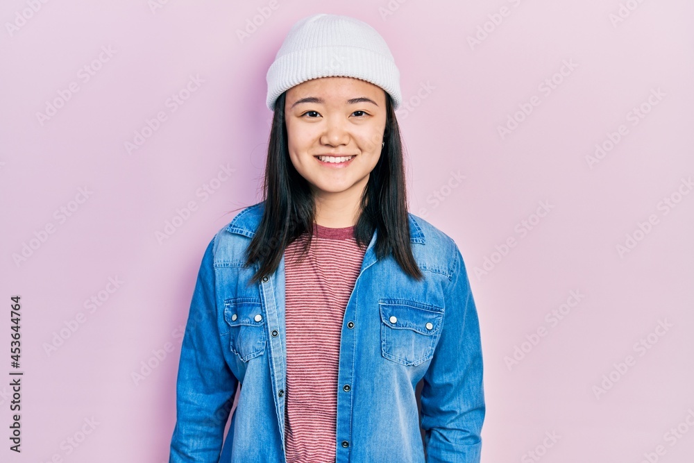 Young chinese girl wearing cute wool cap looking positive and happy standing and smiling with a confident smile showing teeth Young chinese girl wearing cute wool cap looking positive and happy standing and smiling with a confident smile showing teeth