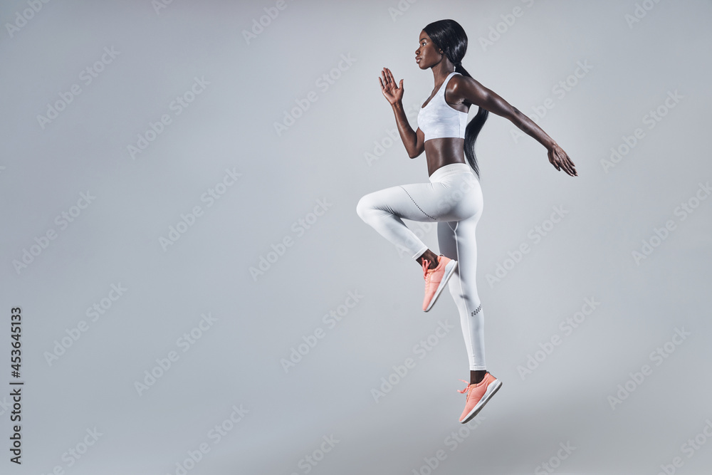 Full length of confident young African woman in sports clothing jumping against gray background