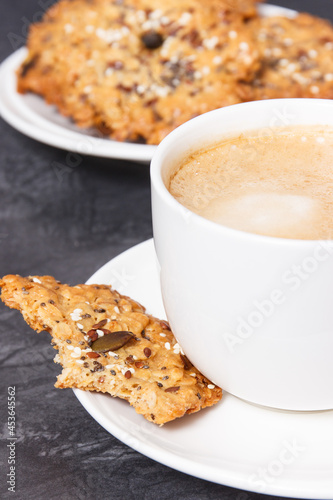 Cup of white coffee and fresh baked oatmeal cookies with honey and healthy seeds. Delicious crunchy dessert