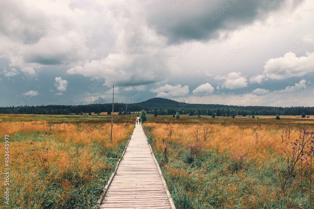 A wooden path leading to the peatbog with view to the hill and clouds above near Bozi Dar, Czech republic