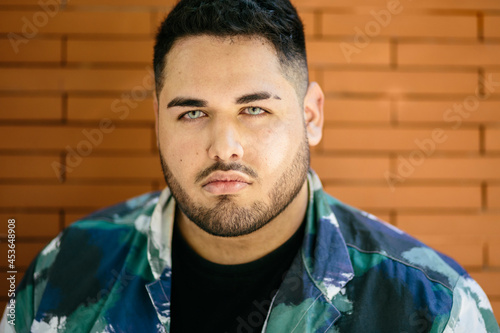 Portrait of a fat latin man with blue eyes, looking at the camera. With a wall of the street in the background. Latins and curvy models concept.