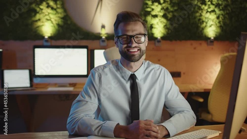 Happy young man looking at camera and smiling while staying late in the office 