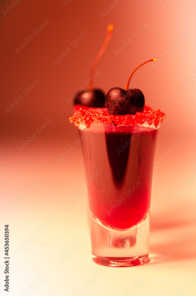 Ruby red cocktail based on vodka, cherry liqueur and syrup in drink shot glass, decorated with fresh cherry and red sugar Ruby red cocktail based on vodka, cherry liqueur and syrup in drink shot glass, decorated with fresh cherry and red sugar