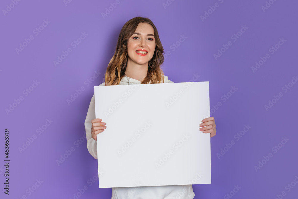 Young caucasian student girl holding a white square sheet of paper in hands smiling isolated on lilac background. Copy space Young caucasian student girl holding a white square sheet of paper in hands smiling isolated on lilac background. Copy space