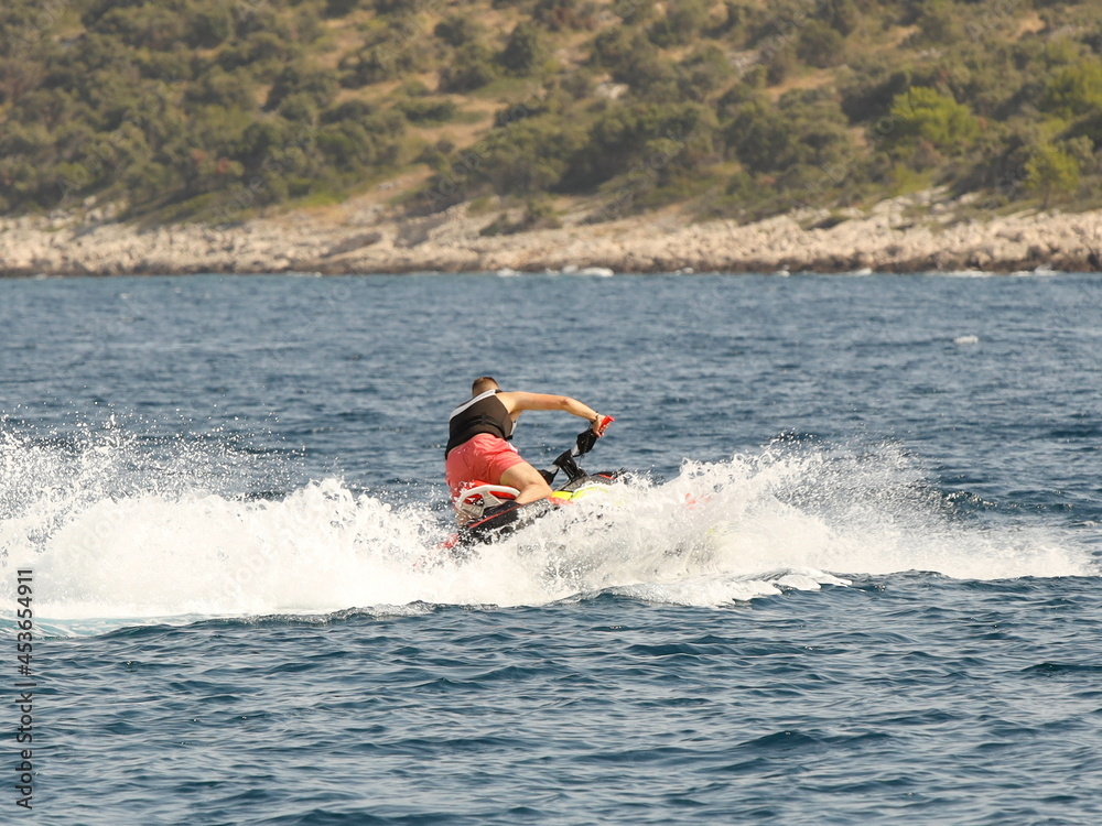 A young guy rides a jet ski on a sunny summer day. An extreme type of transport in nature. Getting adrenaline on your summer vacation. Bends in water transport. Waves and splashes from high speed