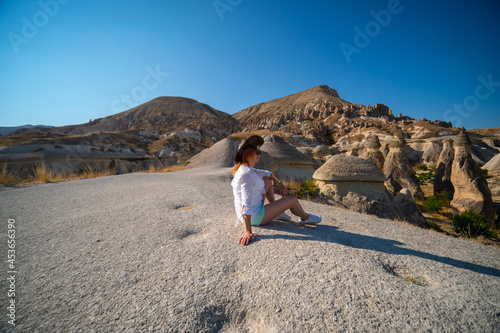 Traveler girl is sitting, tourist posing. Fairy chimneys park in the background. rock formations. Travel and vacation, tour Goreme, Cappadocia, Turkey.