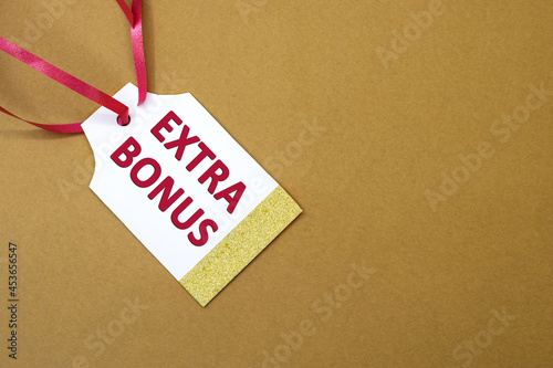 Extra bonus is written in red letters on a white tag for the price tag with a red ribbon. The concept of discounts and sales