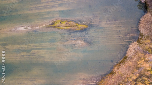 Aerial view shot by a drone of the shore of a forest lake. Thick grass, reflections in the water, green birches in the distance on the slope. Nature of the Blakheide, Beerse, Belgium. High quality photo