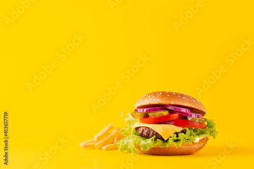 Burger or cheeseburger with a marble beef patty and French fries on a yellow background. Space for text.