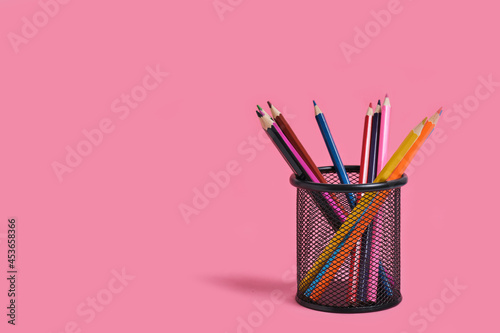 Office basket with colored pencils on a pink background. photo