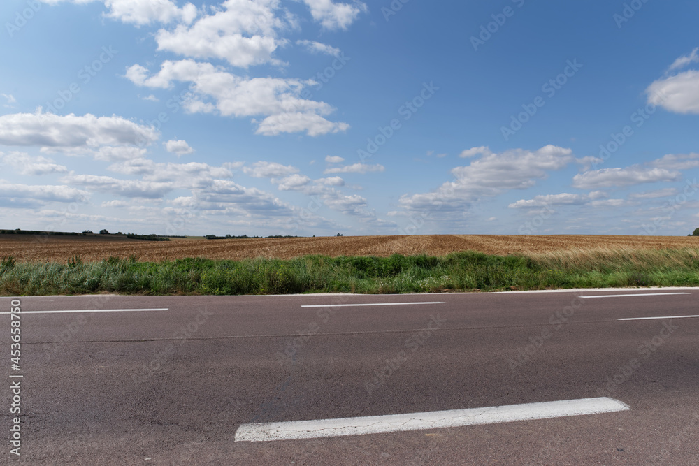 Fototapeta premium Country road and wheat field in Ile-de-France country. Mortery village