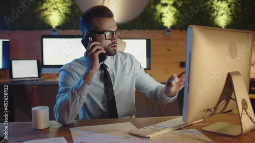 Confident young man working on computer and talking on mobile phone 