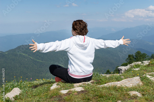 Young woman in sports clothers and arms outstreched to the sidesis sitting on top og mountain, freedom, relaxation, breathing concepts. photo