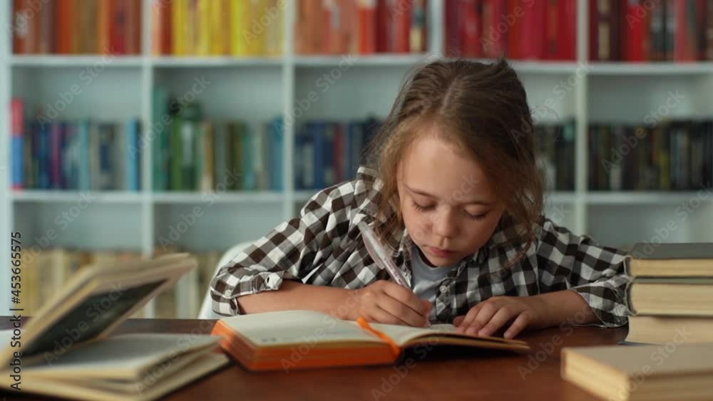 Close-up front view of happy pretty elementary child school girl finishing homework and closing workbook sitting at desk. Adorable smiling primary pupil schoolgirl completing exercise in copybook. Close-up front view of happy pretty elementary child school girl finishing homework and closing workbook sitting at desk. Adorable smiling primary pupil schoolgirl completing exercise in copybook.