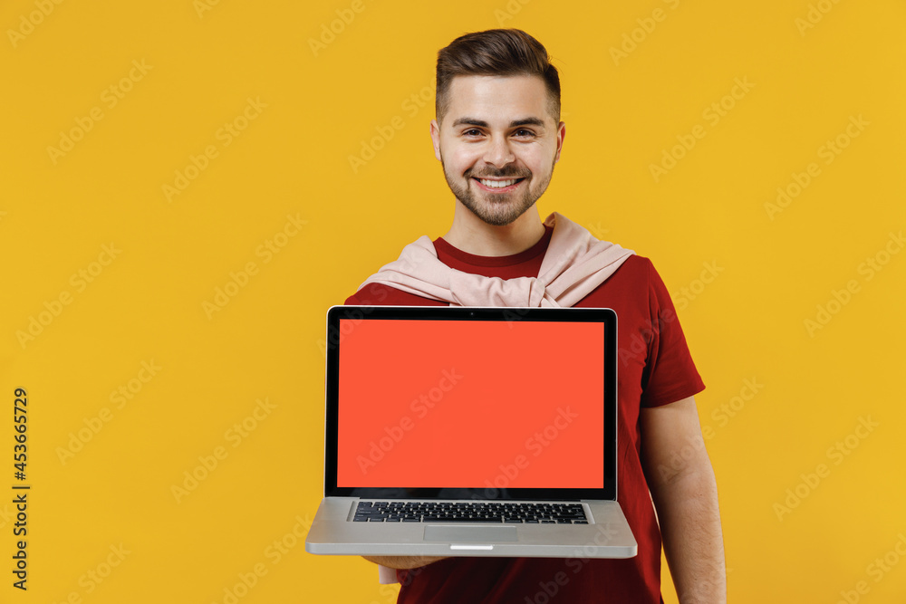 Smiling happy freelancer young man in red t-shirt casual clothes hold use work on laptop pc computer with blank screen workspace area isolated on plain yellow color wall background studio portrait Smiling happy freelancer young man in red t-shirt casual clothes hold use work on laptop pc computer with blank screen workspace area isolated on plain yellow color wall background studio portrait