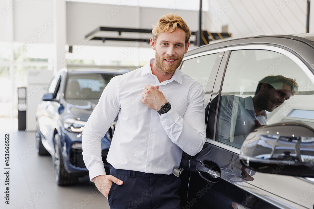 Confident happy man customer buyer businessman client wears white shirt chooses auto wants to buy new automobile in car showroom vehicle salon dealership store motor show indoor. Car sales concept Confident happy man customer buyer businessman client wears white shirt chooses auto wants to buy new automobile in car showroom vehicle salon dealership store motor show indoor. Car sales concept