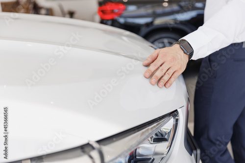 Close up man male arm customer buyer client wearing white shirt chooses auto wants to buy new automobile touch glossy hood in showroom vehicle salon dealership store motor show indoor Sales concept.