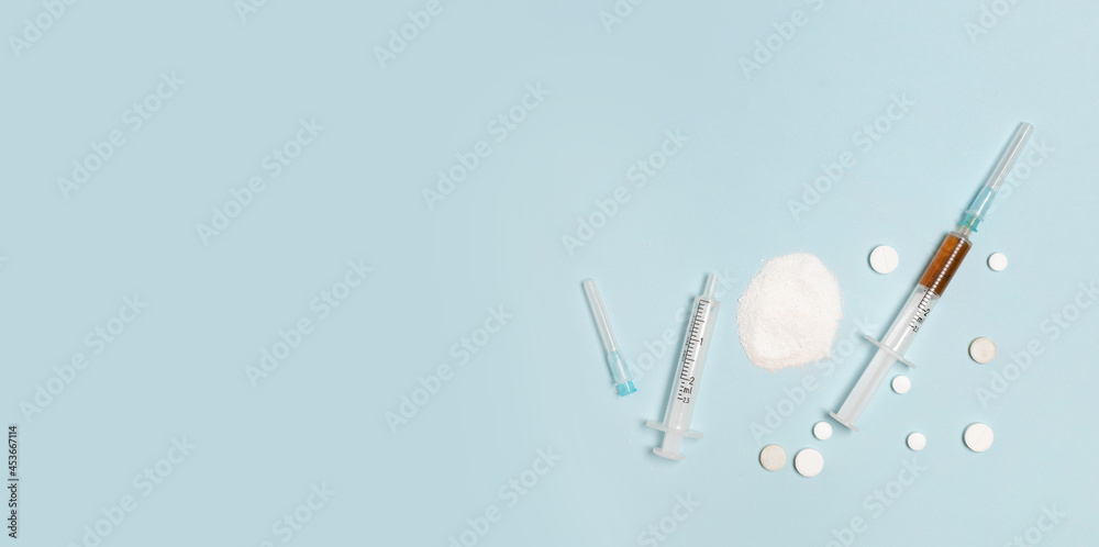International day against drug abuse. Medical preparations powder or capsules of different colors, syringe with injection of drug heroin on blue background. International day against drug abuse. Medical preparations powder or capsules of different colors, syringe with injection of drug heroin on blue background.