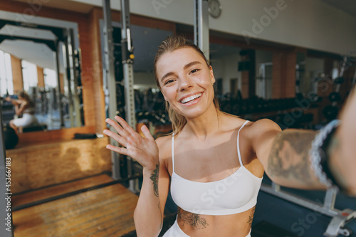 Close up young sporty athletic sportswoman woman in white sportswear warm up training sit near treadmill trainers do selfie shot on mobile cell phone wave hand in gym indoors Workout sport concept photo