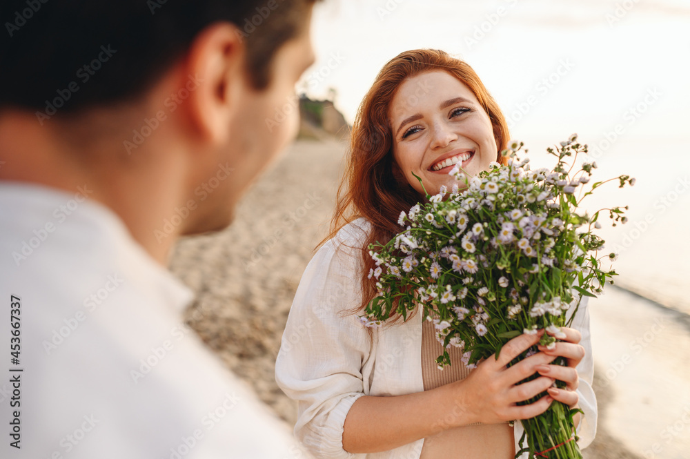 Thankful young satisfied couple family man woman wear white clothes rest relax together boyfriend meet girlfriend gift give bouquet flowers at sunrise over sea sand beach outside seaside in summer day Thankful young satisfied couple family man woman wear white clothes rest relax together boyfriend meet girlfriend gift give bouquet flowers at sunrise over sea sand beach outside seaside in summer day