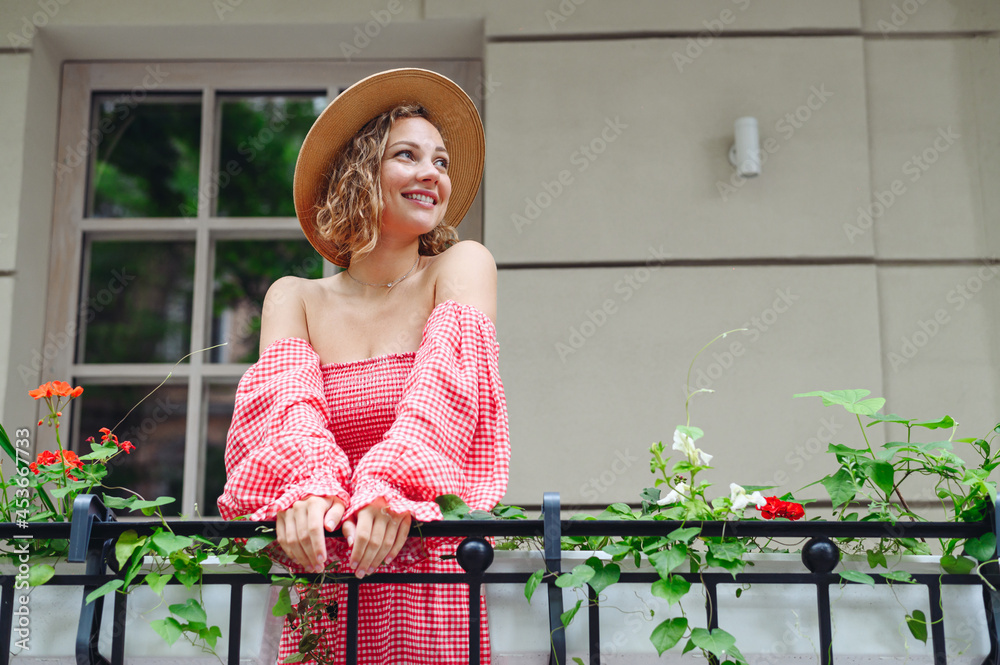 Young dreamful minded smiling happy fun woman 20s wear pink off-the-shoulder dress summer clothes look aside stand on outdoor balcony of town city building People urban summer time lifestyle concept