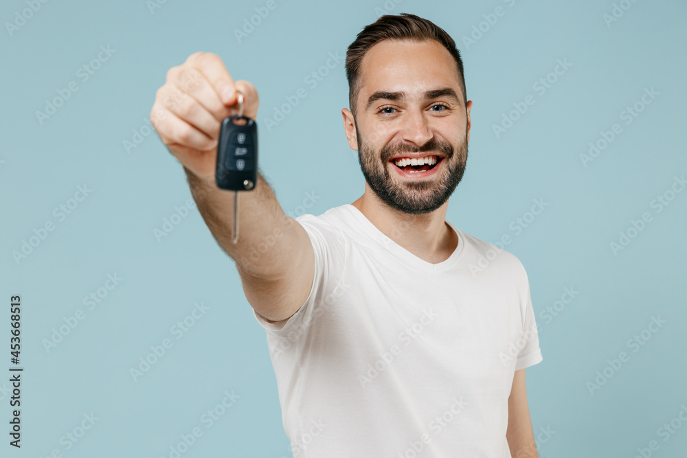 Young smiling happy fun man 20s in casual basic white t-shirt hold in hand giving car key fob keyless system isolated on plain pastel light blue background studio portrait. People lifestyle concept. Young smiling happy fun man 20s in casual basic white t-shirt hold in hand giving car key fob keyless system isolated on plain pastel light blue background studio portrait. People lifestyle concept.