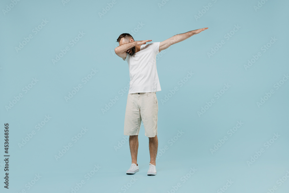 Full length young happy man 20s wearing casual white t-shirt doing dab hip hop dance hands move gesture youth sign hide cover face isolated on plain pastel light blue color background studio portrait. Full length young happy man 20s wearing casual white t-shirt doing dab hip hop dance hands move gesture youth sign hide cover face isolated on plain pastel light blue color background studio portrait.