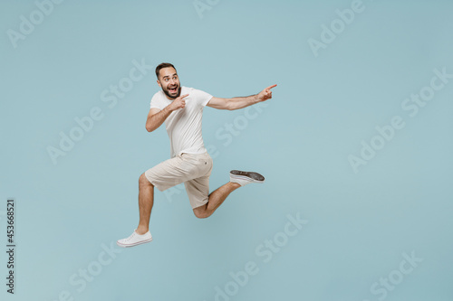 Full length side view young happy man 20s wear casual white t-shirt jump high point index finger aside on workspace area mock up isolated on plain pastel light blue color background studio portrait