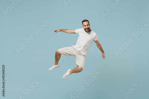 Full length young overjoyed excited smiling happy caucasian man 20s wear casual white t-shirt jump high like flying leaning back isolated on plain pastel light blue color background studio portrait