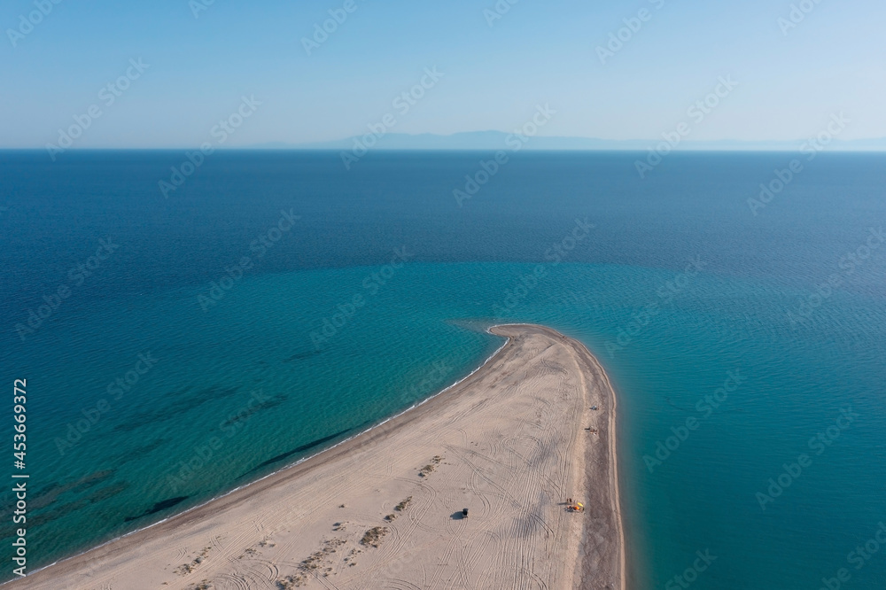 Minimalist aerial view of a long, narrow sandy beach stretching out into a turquoise sea with a mountain silhouette on the horizon