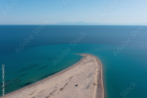 Minimalist aerial view of a long, narrow sandy beach stretching out into a turquoise sea with a mountain silhouette on the horizon