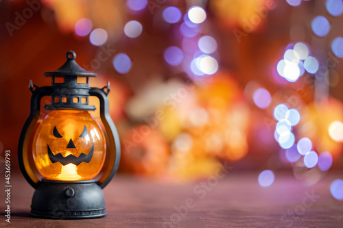 Jack o lanterns Halloween pumpkin face in lantern autumn colored background with bokeh lights and autumn leafs